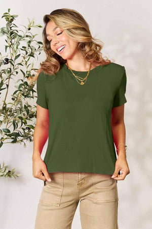 Basic Bae Full Size Round Neck Short Sleeve T-Shirt in green, worn by a woman standing near a plant.