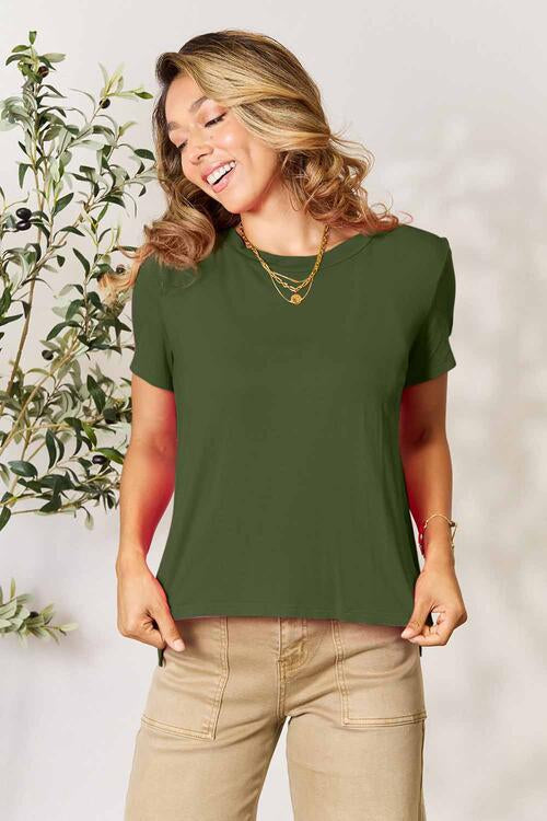 Basic Bae Full Size Round Neck Short Sleeve T-Shirt in green, worn by a woman standing near a plant.