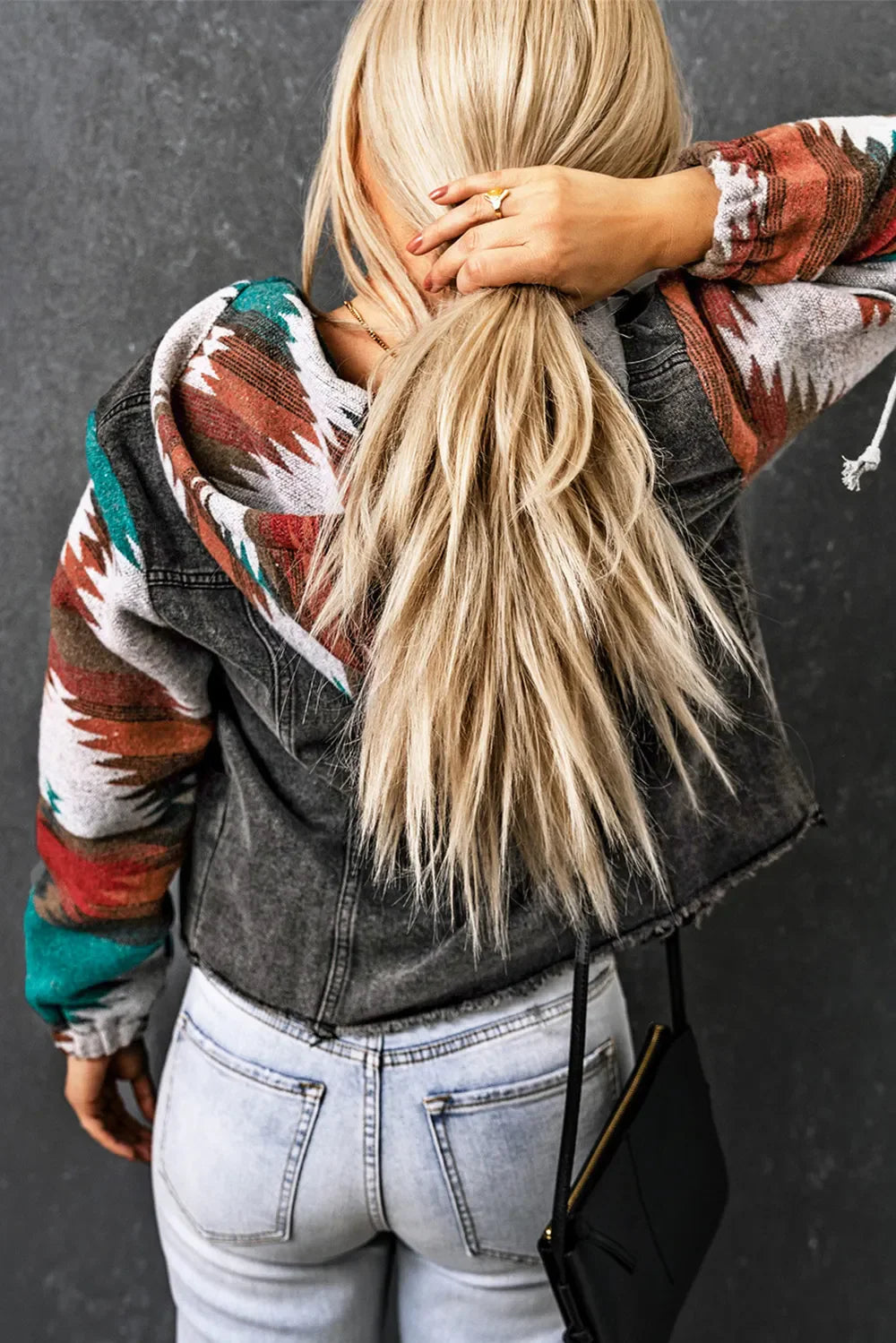 Drawstring hooded pocketed denim jacket with colorful sleeves, worn by woman with long blonde hair.