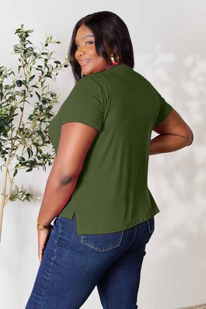 Plus-size model wearing a green Basic Bae Full Size Round Neck Short Sleeve T-Shirt with side slit, paired with blue jeans.