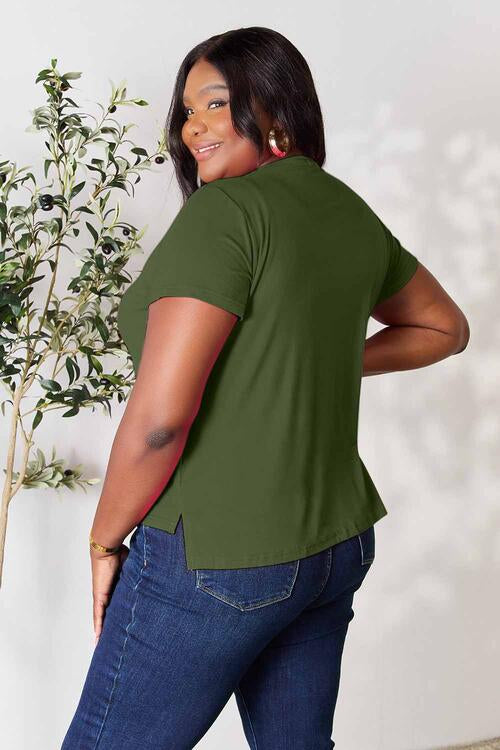 Plus-size model wearing a green Basic Bae Full Size Round Neck Short Sleeve T-Shirt with side slit, paired with blue jeans.