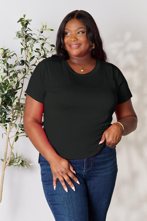 Basic Bae Full Size Round Neck Short Sleeve T-Shirt worn by a woman standing in front of a plant.