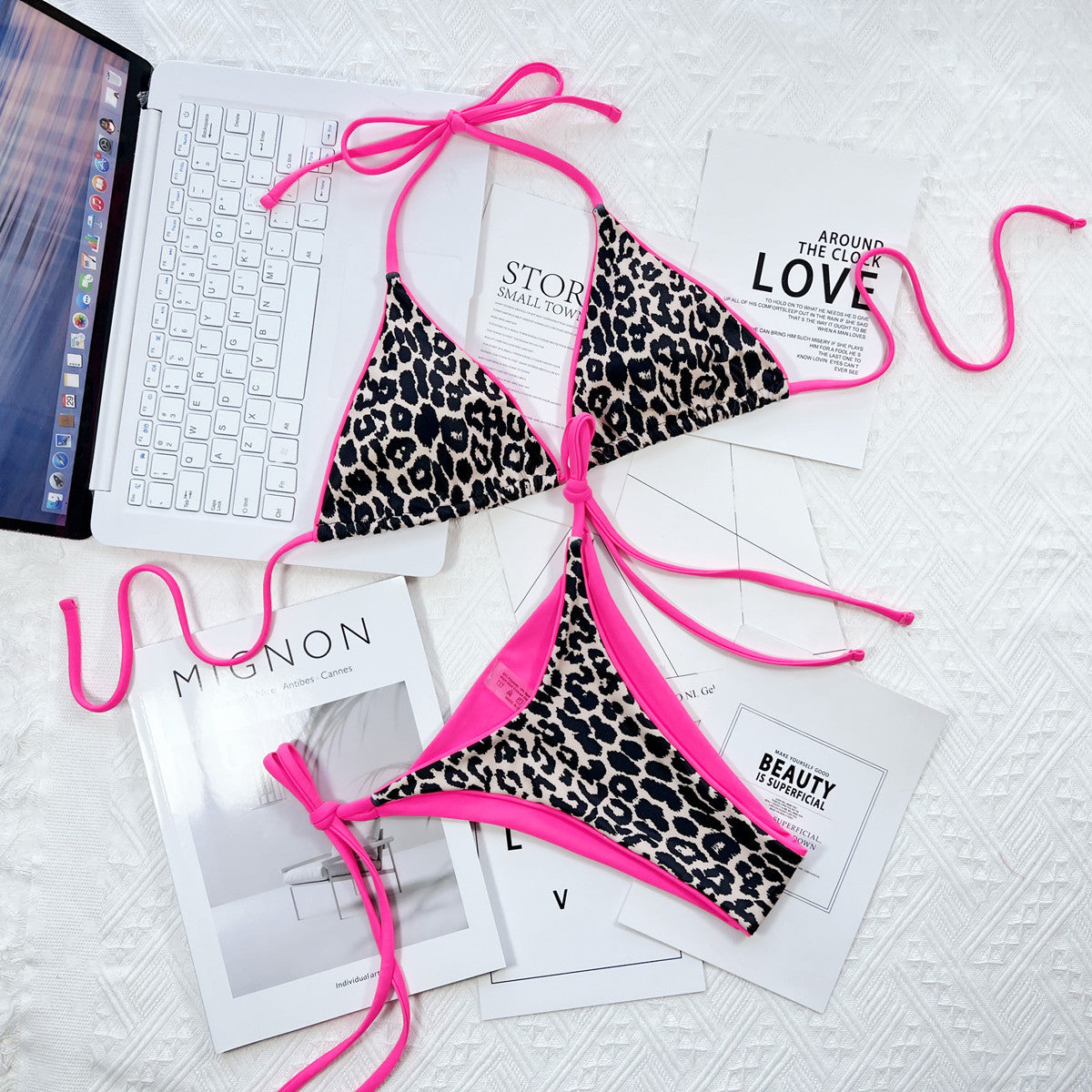 Leopard print halter neck tie side bikini set with pink trim laid on magazines.